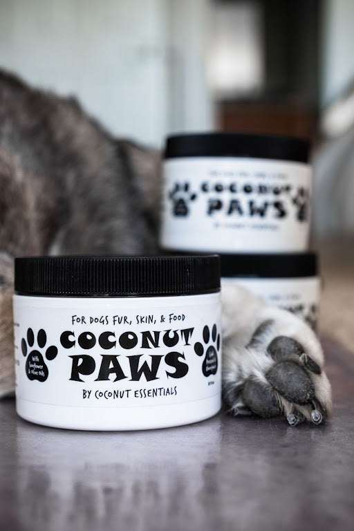 A stack of Coconut Paws tubs near a sleeping dog’s paws.