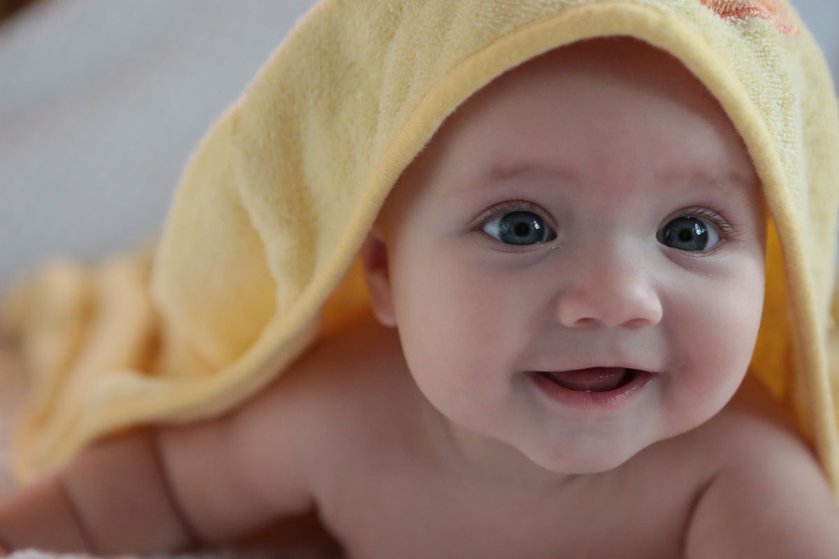 Smiling baby wrapped in a yellow hooded towel after bath time